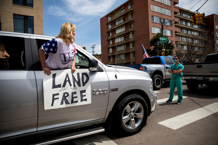 Image: A health care worker stands in the street to counter protest hundreds of others that are demanding the end to stay-at-home orders in Denver on April 19, 2020.