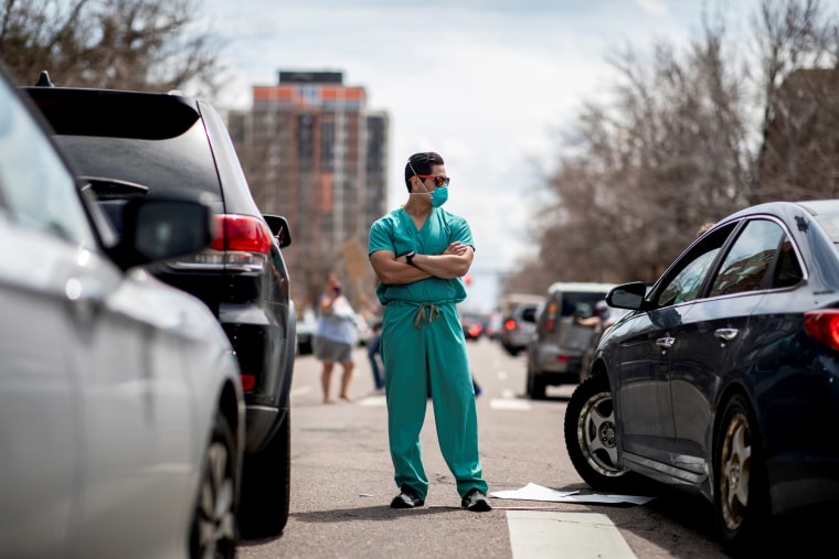 Image: A health care worker stands in the street while protesters demand stay-at-home orders be lifted outside of the State Capitol in Denver on April 19, 2020.