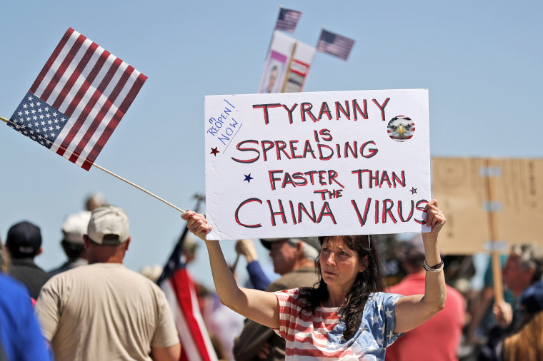 Image: A woman holds a sign as she attends a rally outside the Missouri Capitol to protest stay-at-home orders put into place due to the COVID-19 outbreak Tuesday, April 21, 2020, in Jefferson City, Mo.