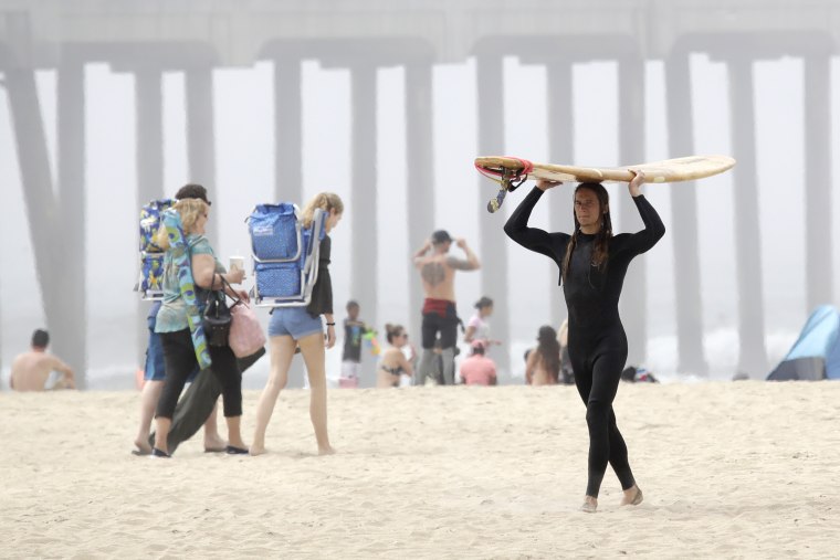 A surfer carries a board Sunday in Huntington Beach, California, as a heat wave lured people to California beaches, rivers and trails, prompting warnings from officials that defiance of stay-at-home orders could reverse progress.