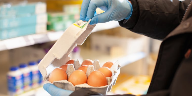Man shopping for eggs at supermarket, wearing protective gloves