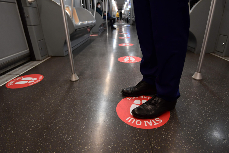 Image: A man stands on a red spot, reading "Stand here," aimed at maintaining distance between commuters in an underground metro line in Milan