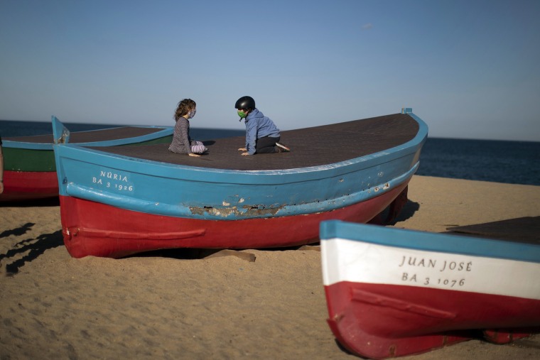 Image: Two children wearing face masks sit on top of a boat in a beach in Badalona, near Barcelona, Spain on Tuesday.