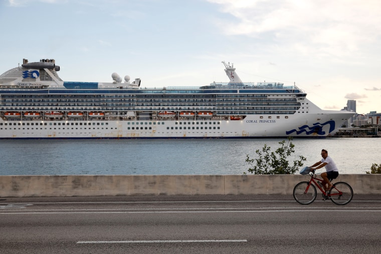 Image: A man rides a bicycle in front of the Coral Princess ship, of Princess Cruises fleet, docked at Miami Port with patients affected by coronavirus disease (COVID-19), in Miami