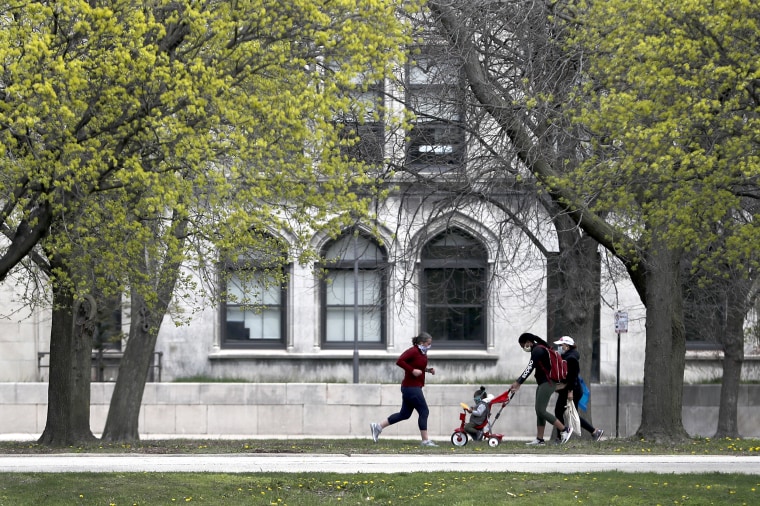 A runner, and two women wearing protective masks pass near the University of Chicago on April 27, 2020, in Chicago.