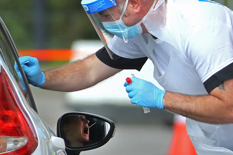 Image: A Medical worker wearing a protective face mask and screen, disposable gloves and a plastic apron, takes a swap at a coronavirus drive-through testing center in the car park of the closed Chessington World of Adventures Resort theme park