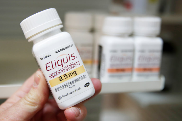 A pharmacist holds a bottle of the drug Eliquis at a pharmacy.