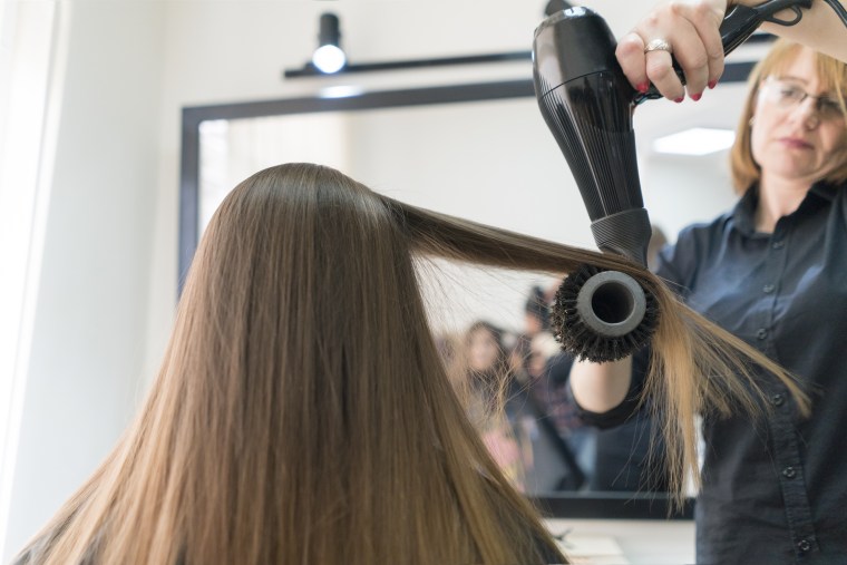 Hairdresser blowing beautiful woman's hair