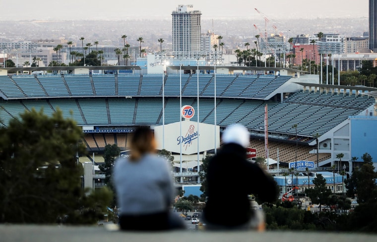 Image: People sit on a hill overlooking the empty Dodgers Stadium in Los Angeles on March 26, 2020.