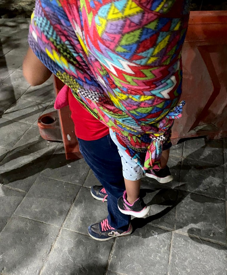 Image: A migrant woman waits with her child on her back