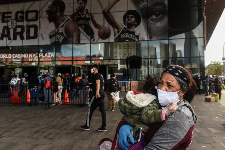 Image: Santa Arias holds her grand daughter as she decides whether to wait on a long line for a food bank donation at the Barclays Center on May 15, 2020 in the Brooklyn borough in New York City.