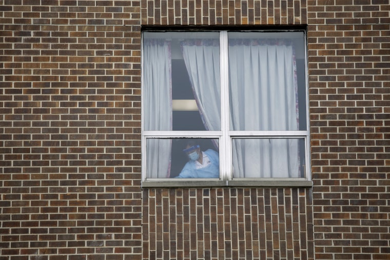 A worker wearing personal protective equipment cleans around a window at the Alden Lakeland nursing home.