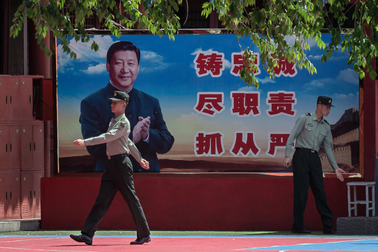 Image: People's Liberation Army soldiers next to a poster of President Xi Jinping 