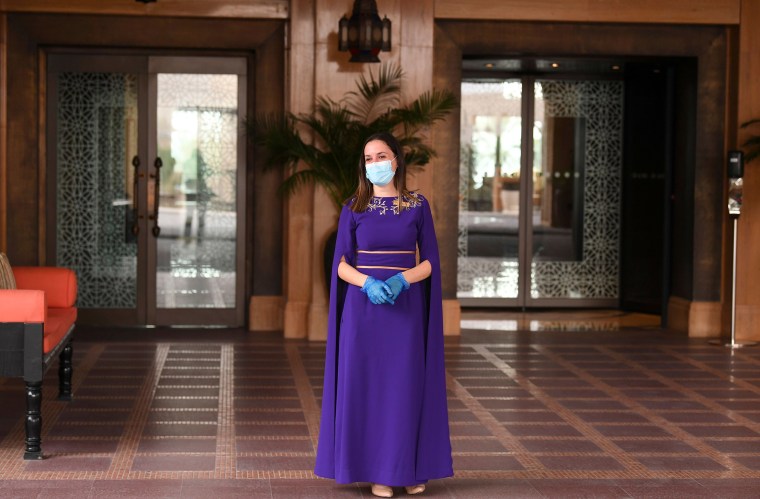 Image: A mask-and-glove-clad staff member of the Jumeirah al-Naseem hotel waits at the hotel reception in Dubai