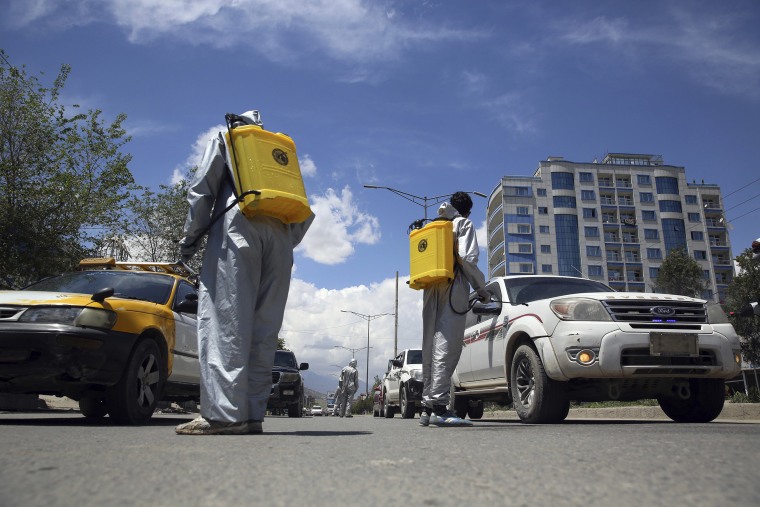 Image: Volunteers in protective suits spray disinfectant on passing vehicles to help curb the spread of the coronavirus in Kabul, Afghanistan