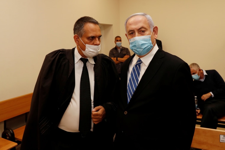 Image: Israeli Prime Minister Benjamin Netanyahu, wearing a mask, stands inside the courtroom as his corruption trial opens at the Jerusalem District Court