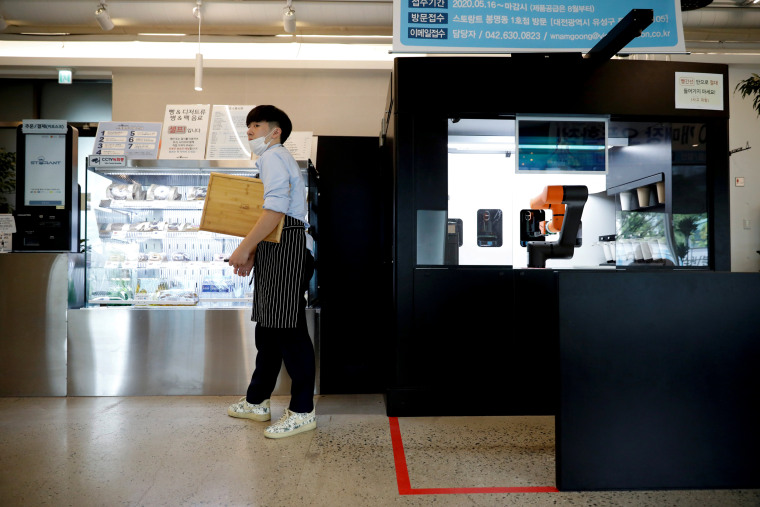 Image: An employee stands next to a robot barista that takes orders, makes coffee and brings drinks to customers in Daejeon, South Korea, on May 25, 2020.
