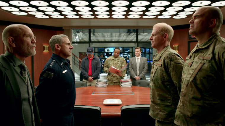 John Malkovich as Dr. Adrian Mallory, Steve Carell as General Mark. R. Naird, Alex Quijano as Steve Hines, Roy Wood Jr. as Army Liaison Bert Mellows, John Hartmann as Chambers, Noah Emmerich as Kick Grabaston, and Brandon Molale as Clarke Luffinch in episode 105 of "Space Force" on Netflix.
