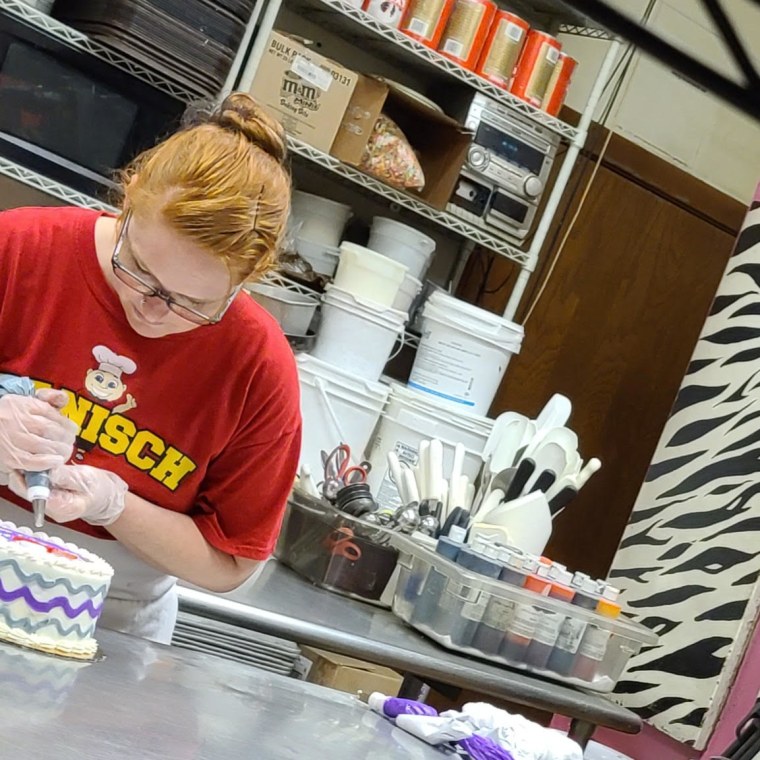 A bakery worker decorates a cake with buttercream frosting.
