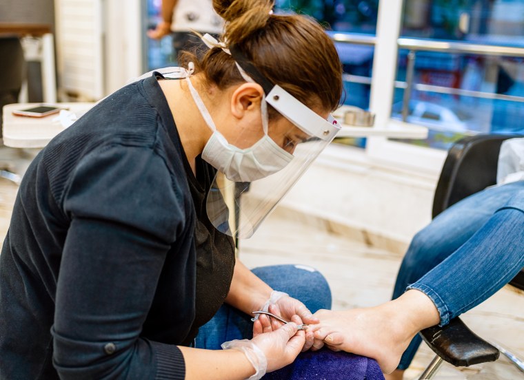 Woman with protective face mask on manicure treatment in beauty salon