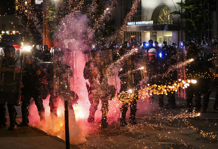 Image: Fireworks go off in front of police, who with protesters in front of police headquarters in St. Louis