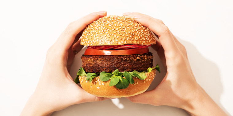 cropped view of woman holding delicious vegan burger with radish on white background