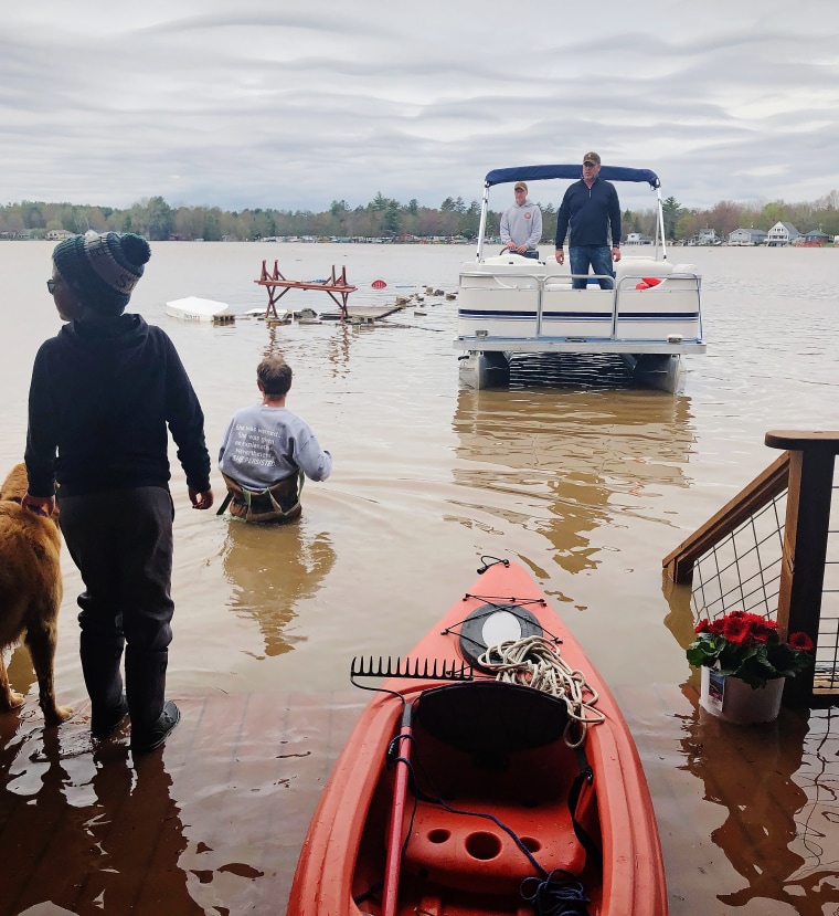 A man in a pontoon boat rescues the Lackey and Schulz families from their lakefront homes.