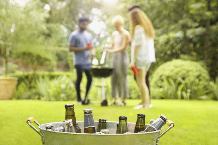 Beer bottles in bucket while friends enjoying barbecue party in background at yard