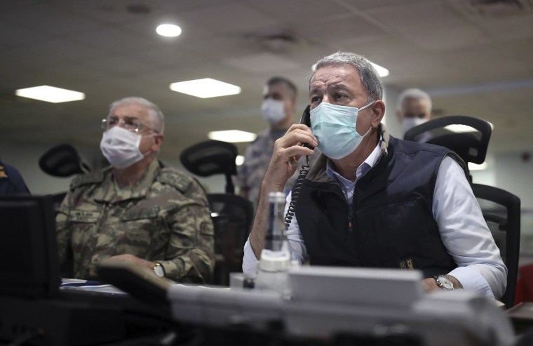 Image: Turkish Defense Minister Hulusi Akar, right, and Chief of Staff Gen. Yasar Guler wearing face masks to protect against the coronavirus, monitor the operation at a military headquarters in Ankara, Turkey