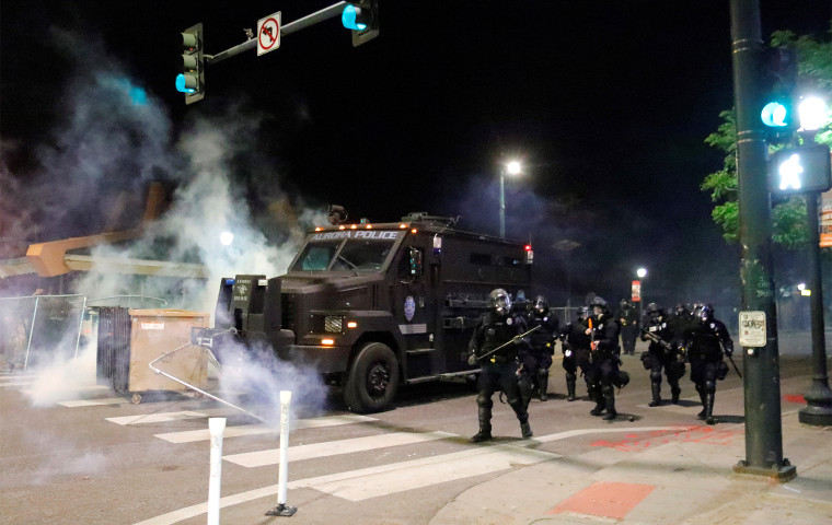 Armed police officers cross an intersection next to a military vehicle belonging to the Aurora Police Department during a protest in Denver on May 31, 2020.