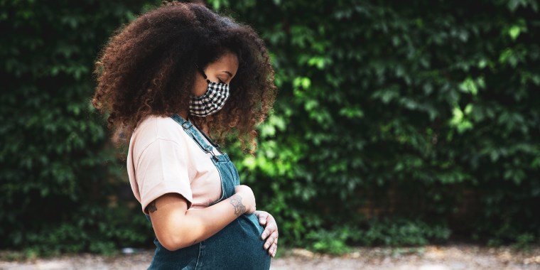 Pregnant afro hair woman in the city wearing a cloth protective mask