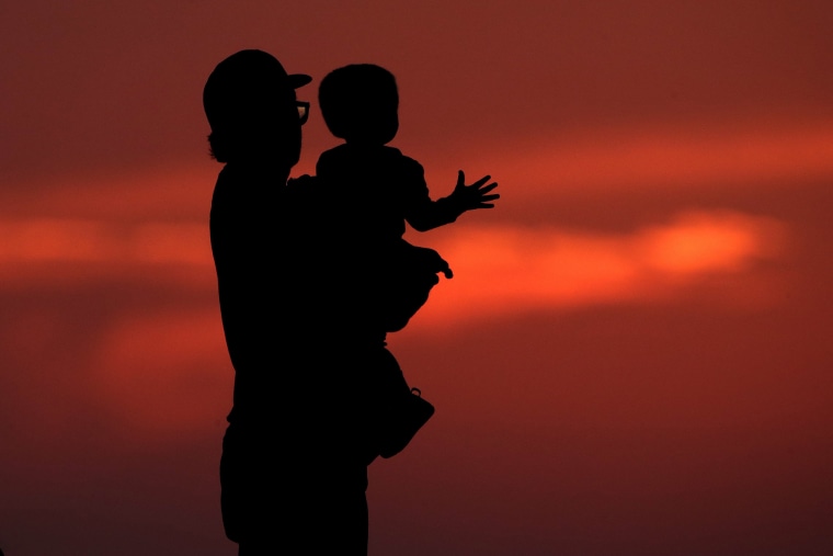 A man and his son are silhouetted against the sky as they watch the sunset from a park in Kansas City, Mo., Friday, June 26, 2020. Sunsets and sunrises are more vibrant than usual lately due to dust in the atmosphere from a Saharan dust cloud.