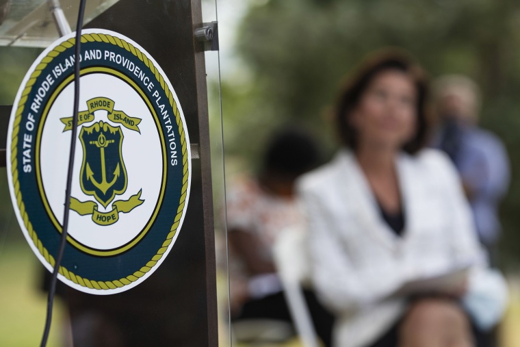 Image: The seal of the State of Rhode Island decorates a podium as Gov. Gina Raimondo looks on at right during a news conference where she announced that she has signed an executive order to remove the phrase \"Providence Plantations\" in the state's formal