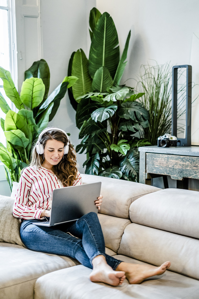 Smiling woman with laptop and headphones sitting on couch