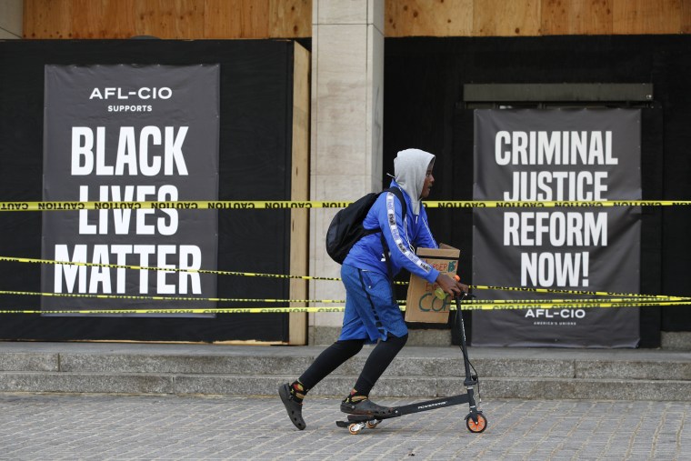 Image: A boy rides a scooter past signs outside the boarded-up entrance to AFL-CIO headquarters in Washington