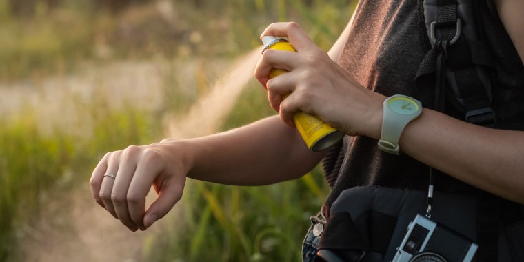 Woman using anti mosquito spray outdoors at hiking trip.