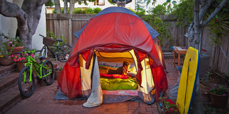 boy reading in tent in side yard of house