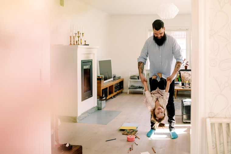 Mid adult father swinging cheerful daughter in living room at home