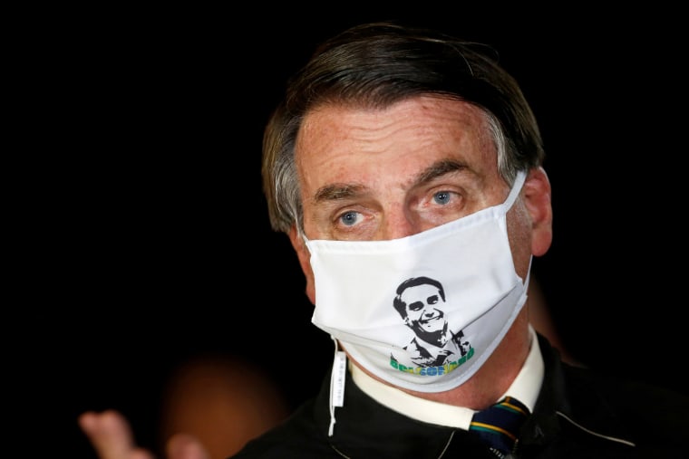 Image: Brazil's President Jair Bolsonaro speaks with journalists while wearing a protective face mask as he arrives at Alvorada Palace