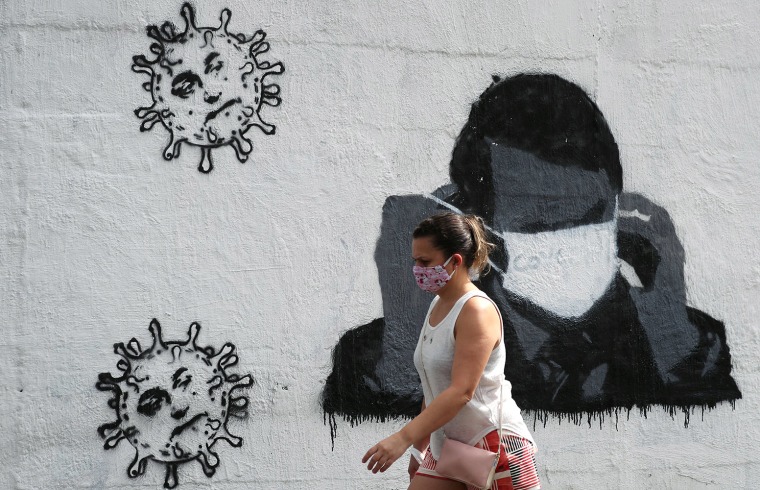 Image: A woman walks past by a graffiti depicting Brazil's President Jair Bolsonaro adjusting his protective face mask and viruses, amid the coronavirus disease (COVID-19) outbreak in Rio de Janeiro, Brazil