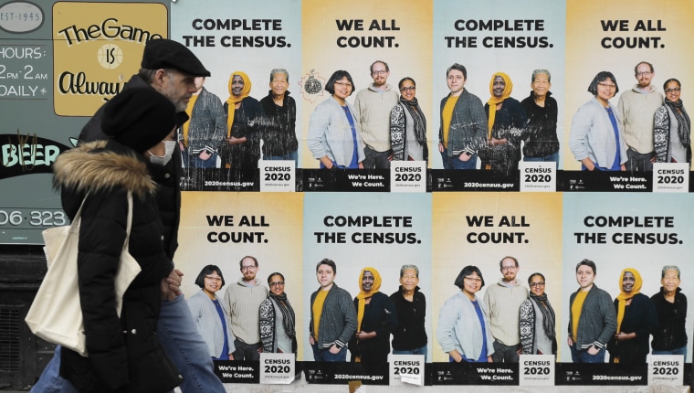 Image: People walk past posters encouraging participation in the 2020 Census in Seattle