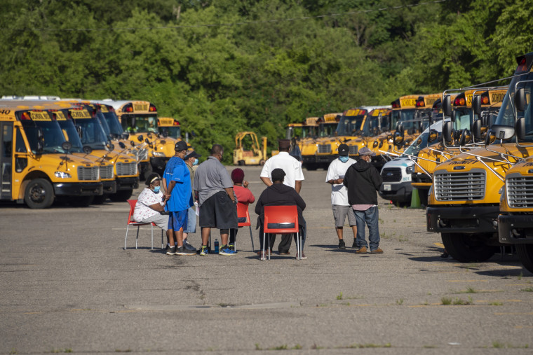 Workers sit amid dozens of idle school buses after demonstrators blocked the driveways of the Detroit Public Schools West Side Bus Terminal on the first day of summer school on Monday. 
