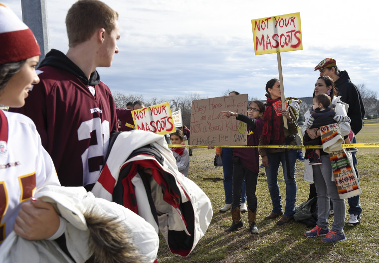 Fans of the Washington football team walk past as Native Americans and supporters protest the team's name and logo before the game on Dec. 28, 2014.