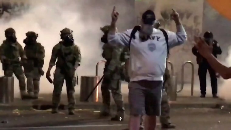 Image: A man wearing a "NAVY" shirt gestures to a police officer after being sprayed and beaten during a protest against racial inequality in Portland,