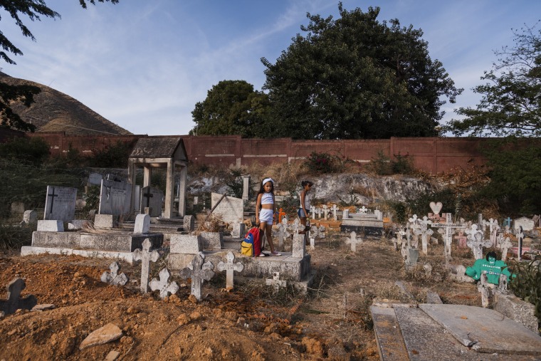 A santera girl cries in front of a mass grave as a family member is buried in Carabobo, Venezuela, on March 30, 2018. The smell of the decomposed body was so strong that family members had to keep distance from the pits during the burials.