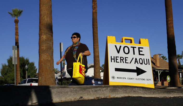 Image: A woman walks past a sign directing voters to a polling place in the Phoenix