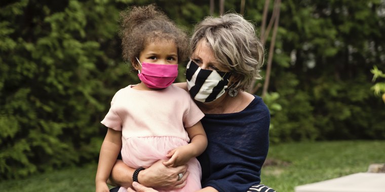Grandmother holding toddler granddaughter with protective mask.