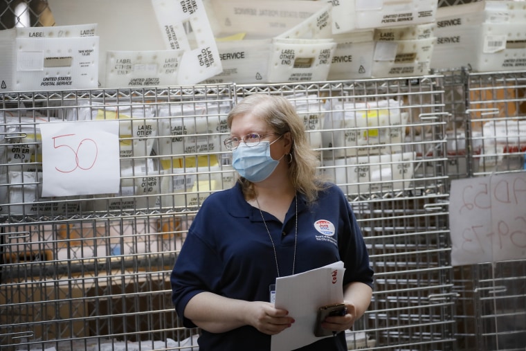 Cages loaded with ballots in U.S. Postal Service bins rest behind a worker at a Board of Elections facility in New York City on July 22, 2020.