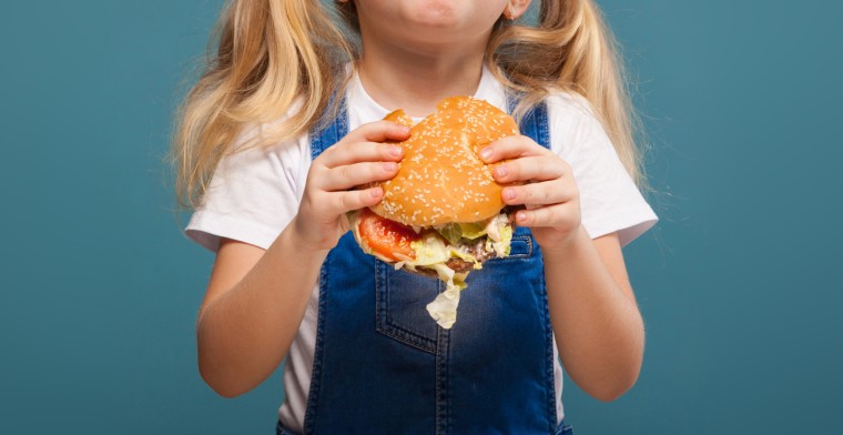 Adorable cute little girl in white shirt and jean jumpsuit with hamburger