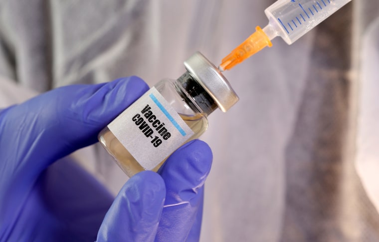 Image: A woman holds a small bottle labeled with a \"Vaccine COVID-19\" sticker and a medical syringe.